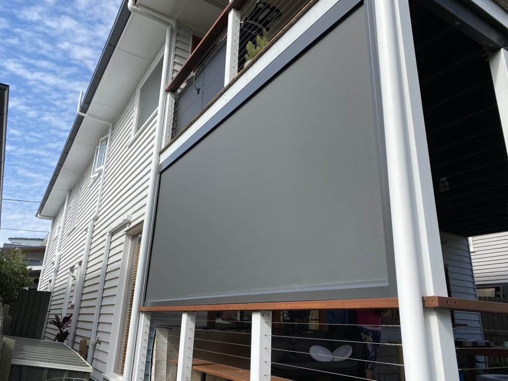 Two-story house with white siding and retractable gray shade.