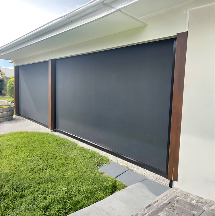 Two large, dark outdoor roller blinds are installed on the side of a white building near a green lawn and stone path.