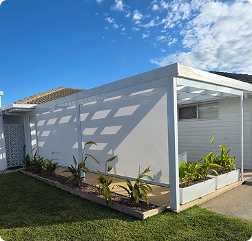 A white pergola with a raised garden bed and young plants stands beside a single-story house under a partly cloudy sky.