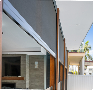 Outdoor retractable shades installed on a modern balcony, partially rolled down, with a view of a living room and palm trees visible outside.