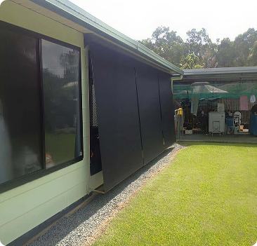 Side view of a house with large black screens covering the windows, next to a green lawn and a shed in the background.