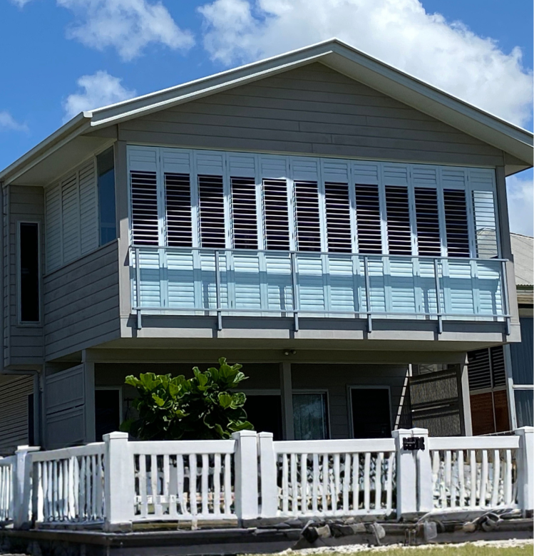 alluminim Two-story house with white shutters on upper windows, a light blue balcony railing, and a white fence in front, under a partly cloudy sky.