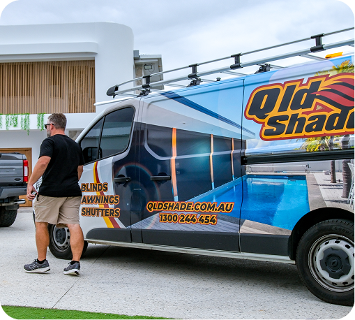 A person walks beside a QLD Shade van displaying company branding and contact info, parked outside a modern house.