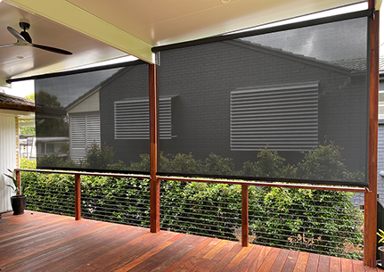 Outdoor patio with wooden floor, wire railing, and a roll-down mesh screen partially blocking the view of a neighboring house and garden. Ceiling fan and potted plant are visible.