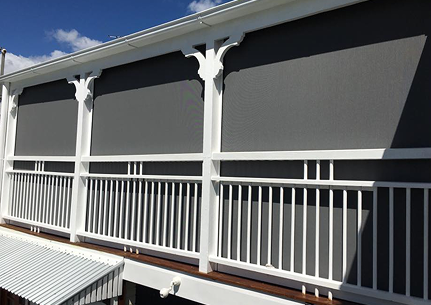 A second-floor balcony with white railings and decorative brackets has large grey outdoor screens covering the openings.