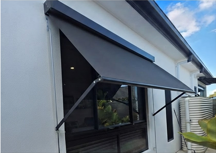 Black retractable awning extended over a window on the exterior of a modern white building, with water tanks visible nearby.