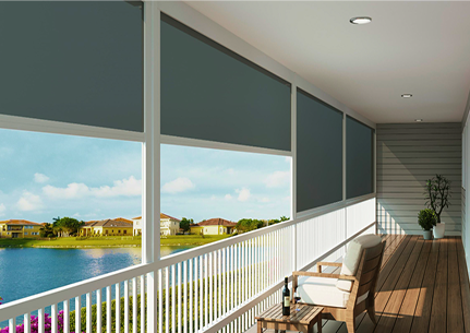 Covered porch with wooden floor, white railing, outdoor seating, potted plant, and roller shades partially covering a view of a lake and houses under a partly cloudy sky.