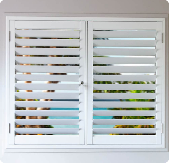 White plantation shutters on a window, with partially open slats revealing a blurred view of palm trees and blue sky outside.