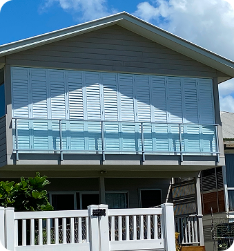 A two-story house with white shutters covering the entire upper balcony, glass balcony railing, and a white fence in front.