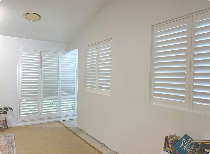 A bright room with white walls and plantation shutters on the windows; a few books are visible in the bottom right corner.