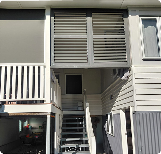 Two-story exterior with a staircase leading to a door, enclosed balcony above, and ground floor area partially visible below.