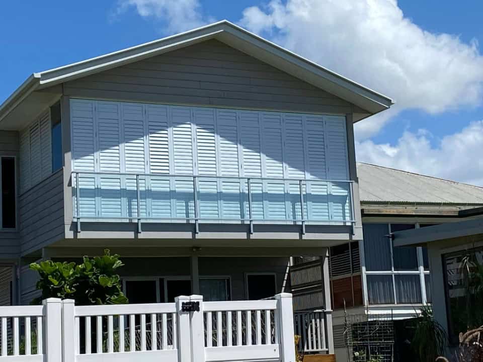 Modern house with aluminum shutters, balcony, and white fence.