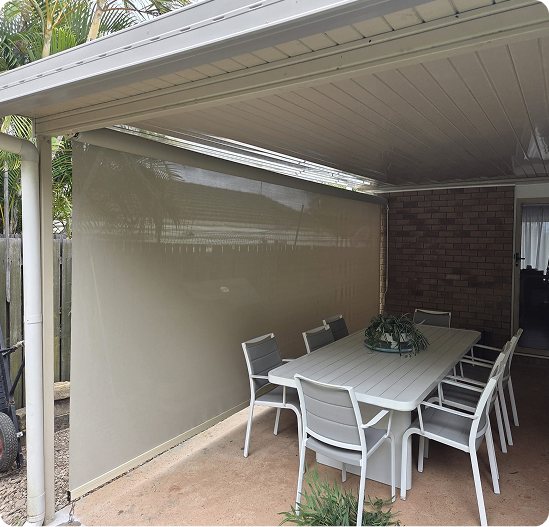 Outdoor patio with a white roof, beige side screen, white dining table, and eight white chairs set on a concrete floor next to a brick wall.