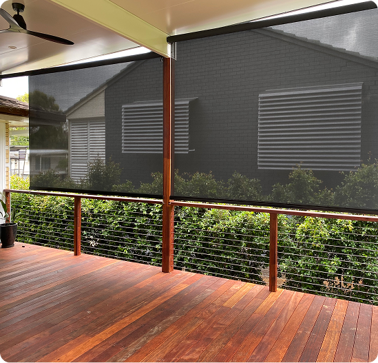 A covered wooden deck with mesh roller blinds partially lowered, overlooking a garden with bushes and a neighboring house visible through the screens.
