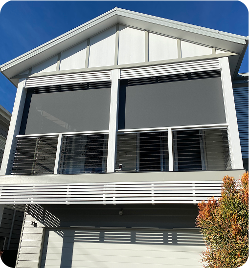 Two large grey outdoor blinds cover the balcony of a modern two-story house with white walls and horizontal railing, under a clear blue sky.