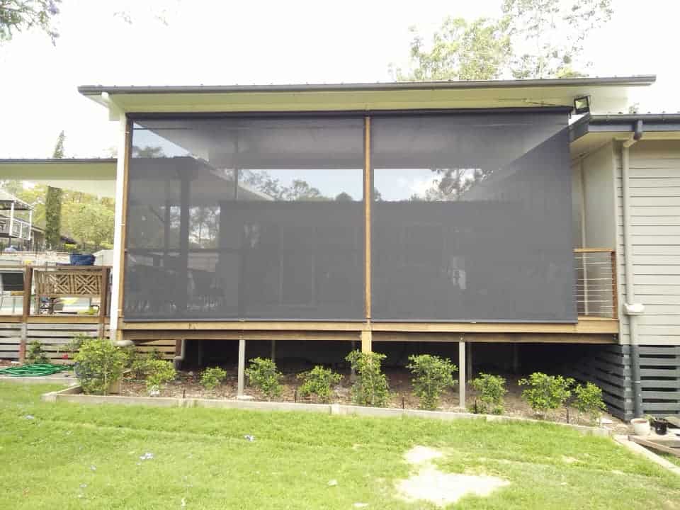 A raised outdoor deck with straight drop mesh blinds covering its open sides, supported by timber posts.