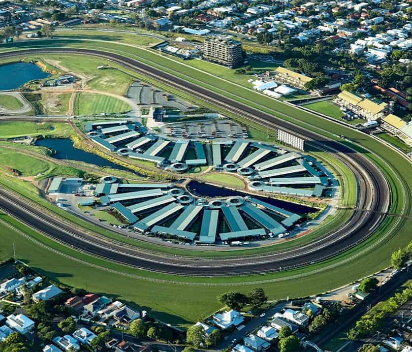 Aerial view of the Ascot horse racing track with stables arranged in a semi-circular pattern inside the course, surrounded by residential and green areas.