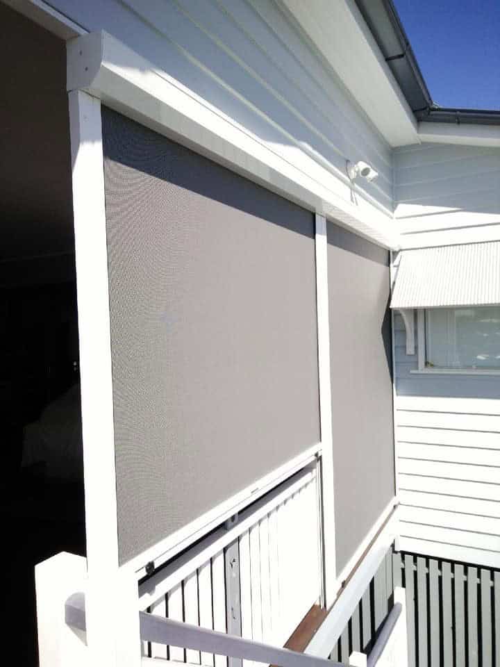 A white house exterior in Shailer Park features two large grey mesh screens covering a veranda, adjacent to a white railing and a window with an awning.
